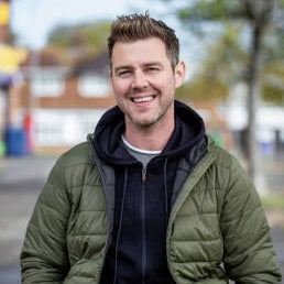 Man wearing a green puffer jacket and black hoodie outdoors